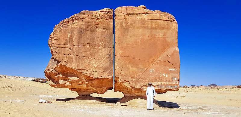 A man stands in front of the Al Naslaa Rock Formation showing its scale