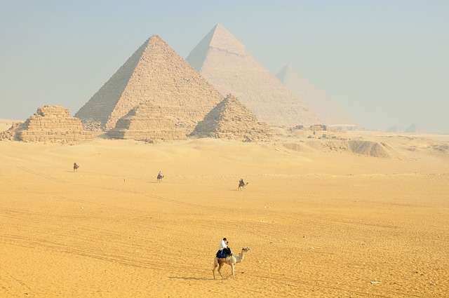 Local guides ride camels past the Pyramids of Giza